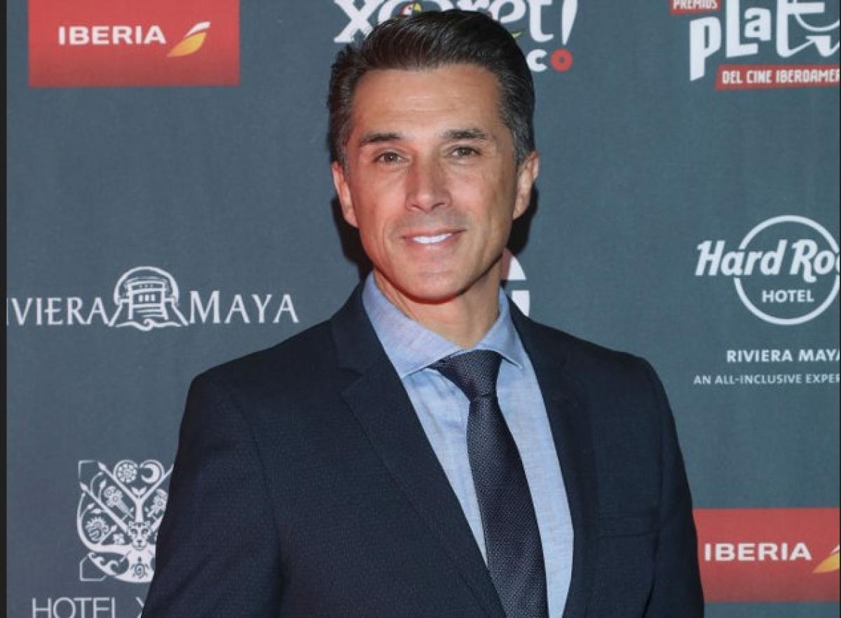 Sergio Mayer poartă o cămașă albastră, cravată, sacou închis la culoare și zâmbește