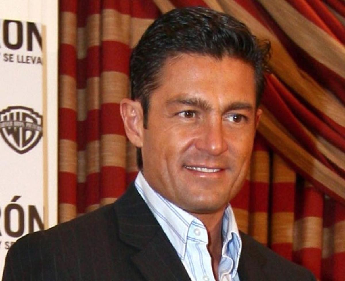 Fernando Colunga poartă o cămașă albastră și un sacou închis la culoare și zâmbește