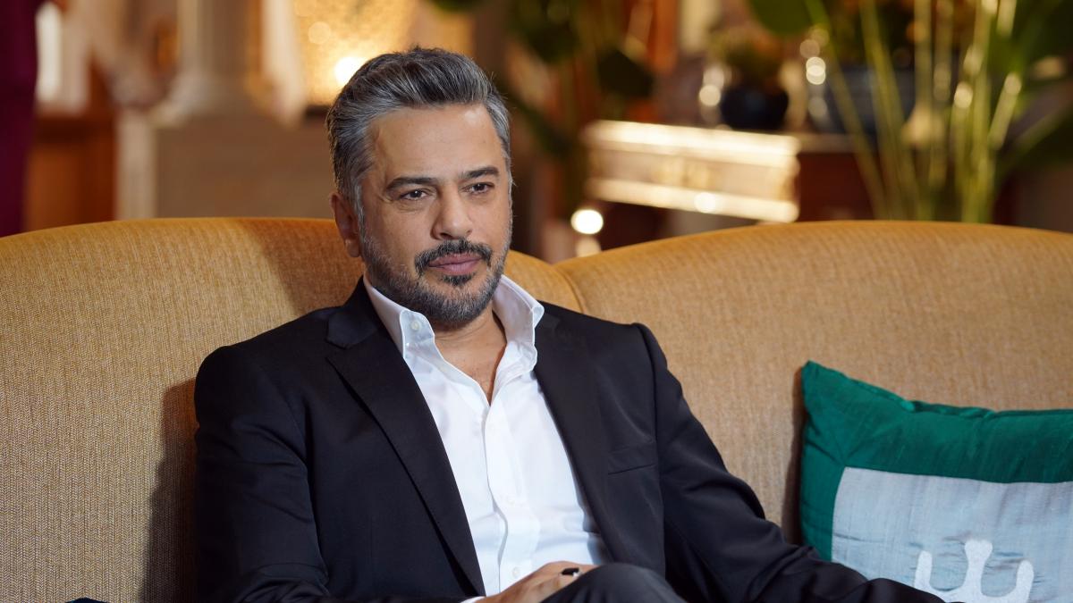 Emre Altuğ poartă o cămașă albă și un sacou negru cu mâneci lungi