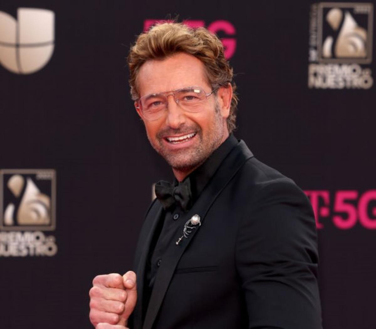 Gabriel Soto poartă ochelari de soare, sacou negru și zâmbește