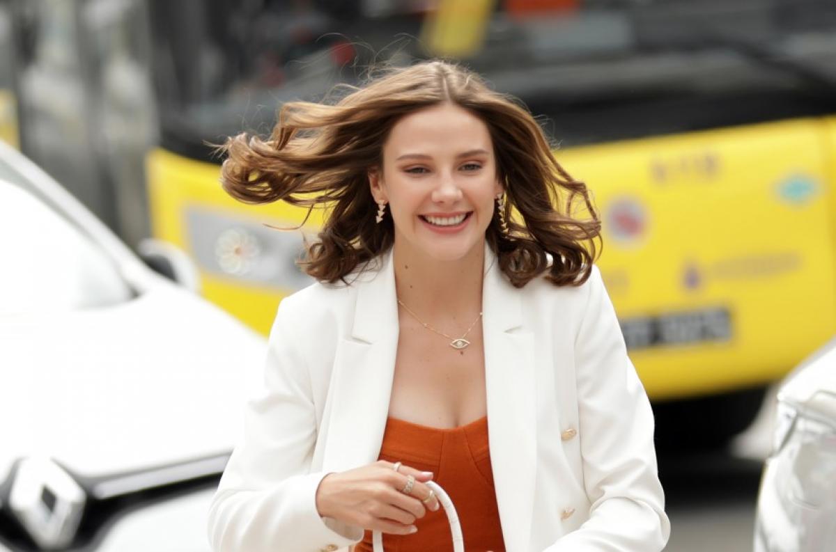 Alina Boz poartă o bluză deschisă la culoare și un sacou alb și zâmbește