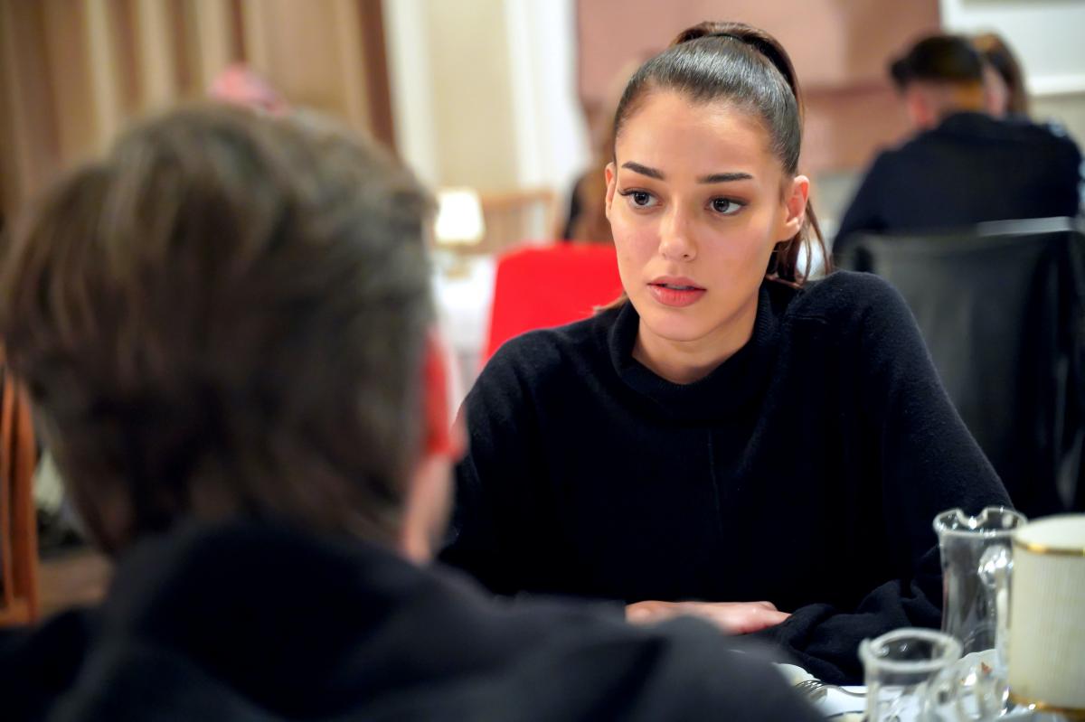 Dilan Çiçek Deniz poartă o bluză neagră cu mâneci lungi, are părul prins în coadă de cal și se uită la cel din fața sa