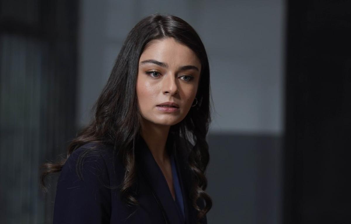 Ayça Ayşin Turan poartă o bluză neagră cu mâneci lungi și are părul desprins, ondulat