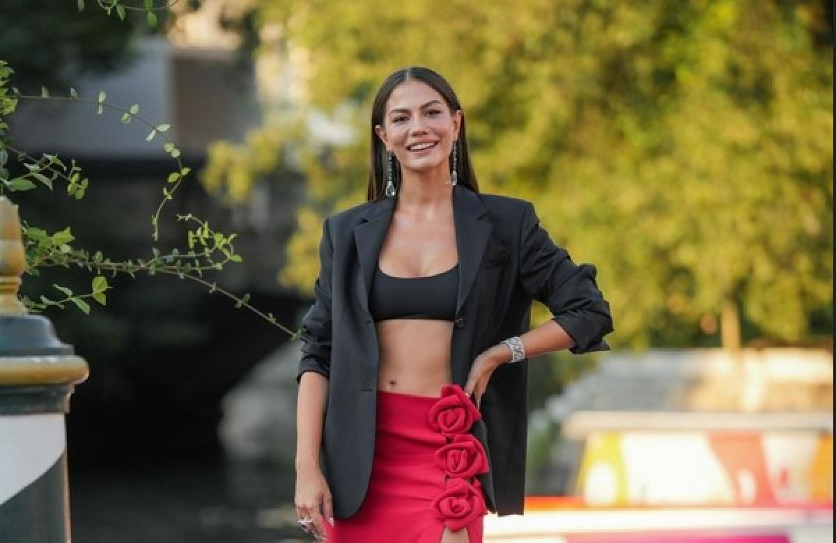 Demet Özdemir poartă un top negru cu fustă roșie și își ține mâna stângă în șold