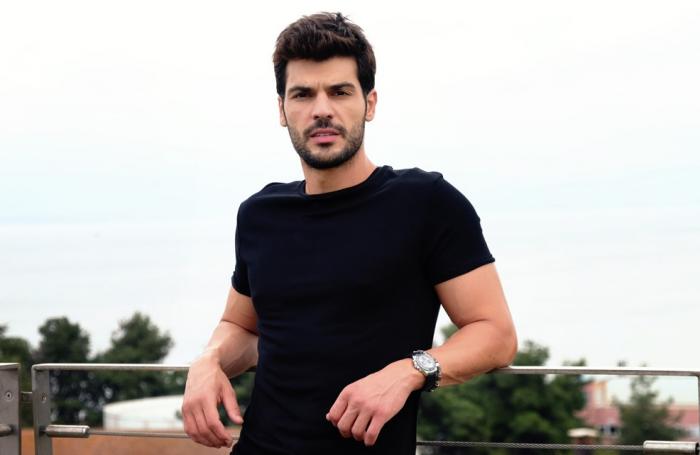 Tolga Mendi poartă un tricou negru și zâmbește