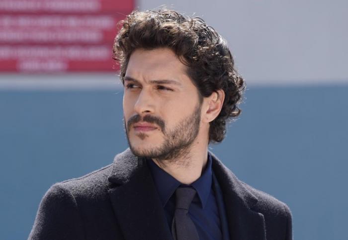 Alperen Duymaz poartă o cămașă închisă la culoare și un palton negru