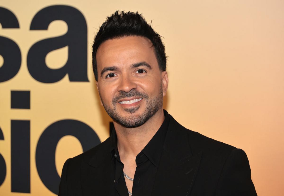 Luis Fonsi poartă o cămașă neagră și zâmbește