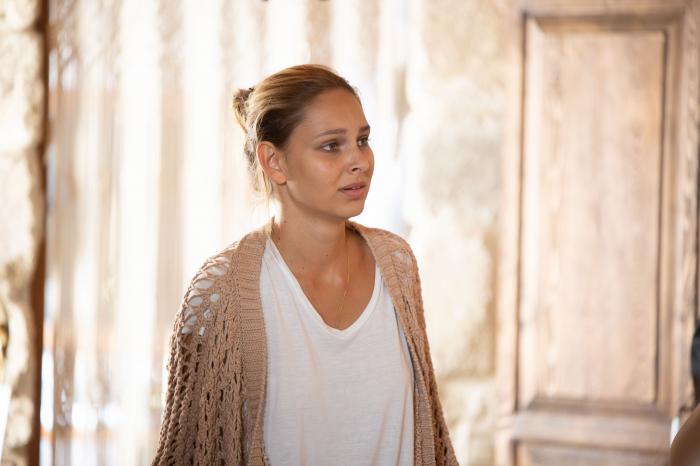 Jessica May poartă un tricou alb și un pulover maro