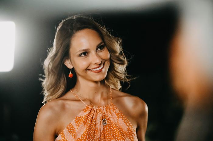 Jessica May poartă o bluză portocalie fără mâneci și zâmbește
