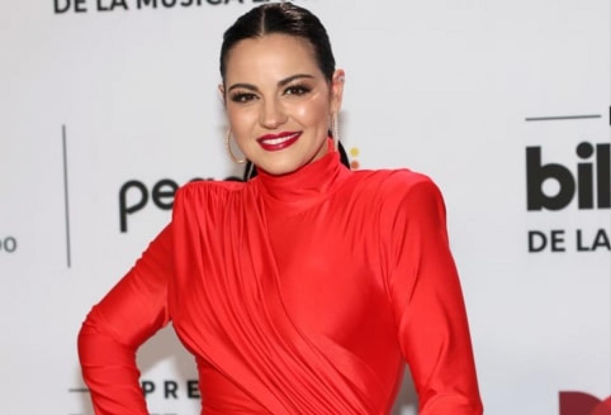 artistă poartă o rochie roșie cu mâneci lungi și zâmbește