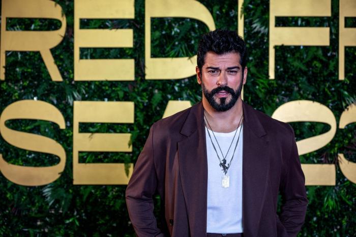 actor poartă o geacă maro și un tricou alb