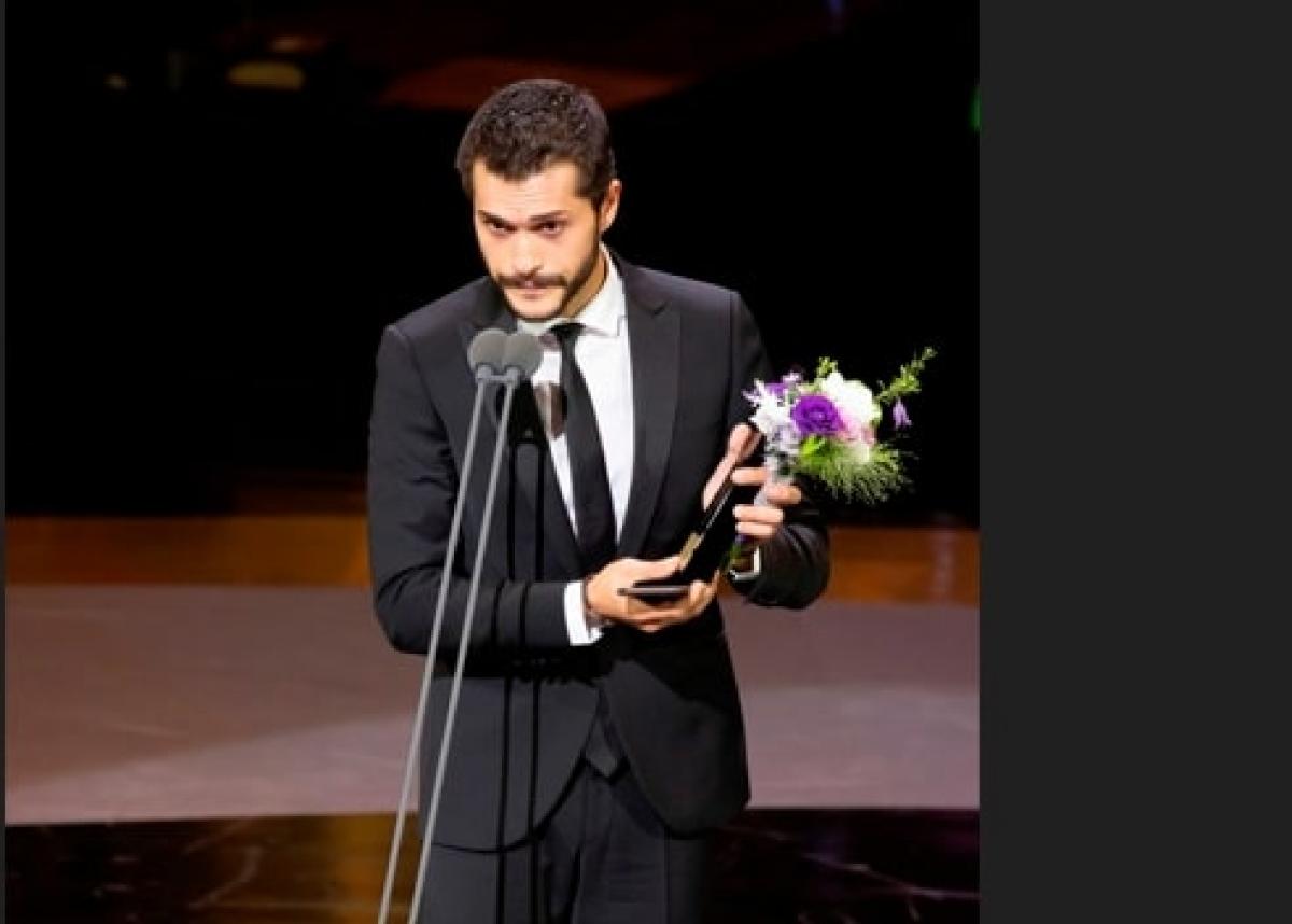 actor poartă costum închis la culoare și vorbește la microfon