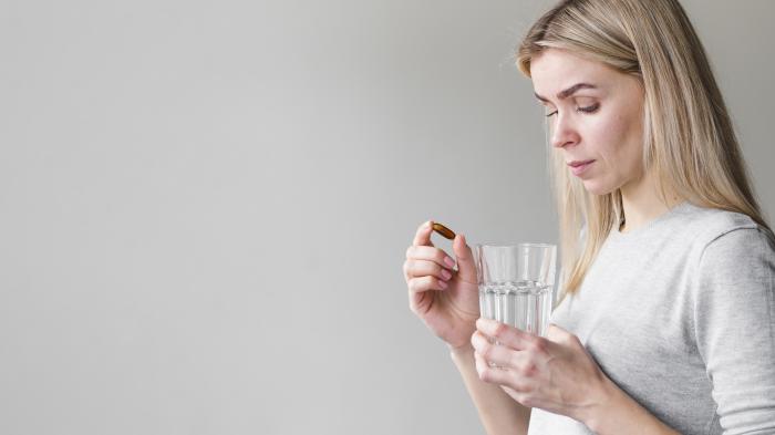 femeie care ține un pahar cu apă în mână și o pastilă