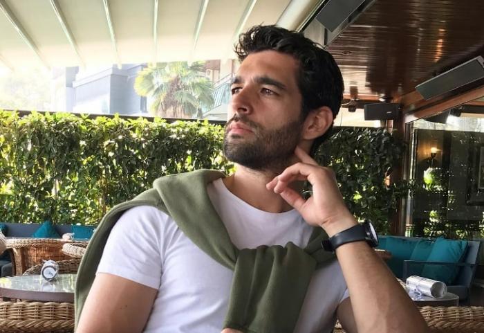 actor poartă un tricou alb și un pulover verde la gât