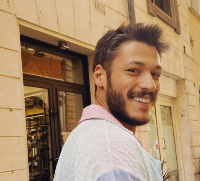 actor poartă o cămașă albă și zâmbește