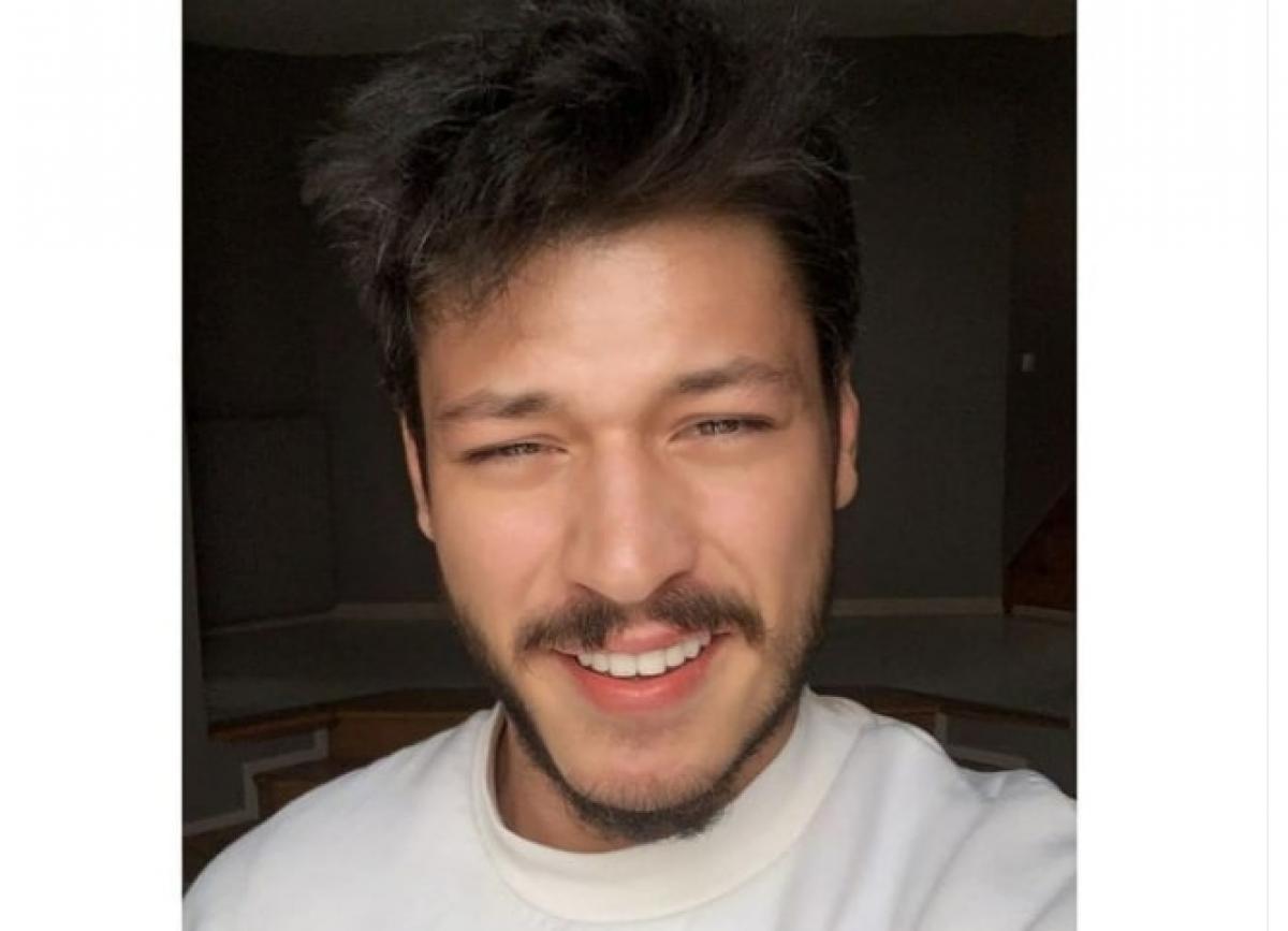 actor poartă un hanorac alb și zâmbește