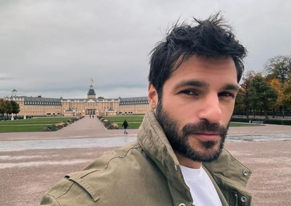 actor poartă un tricou alb și o geacă maro