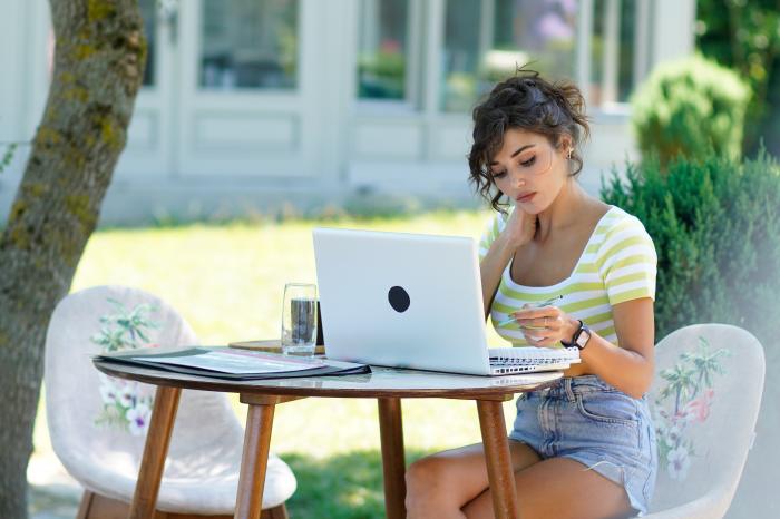 actrița stă în fața unui laptop cu părul prins într-o coadă și cu breton într-o parte și stă pe scaun în fața unei mese