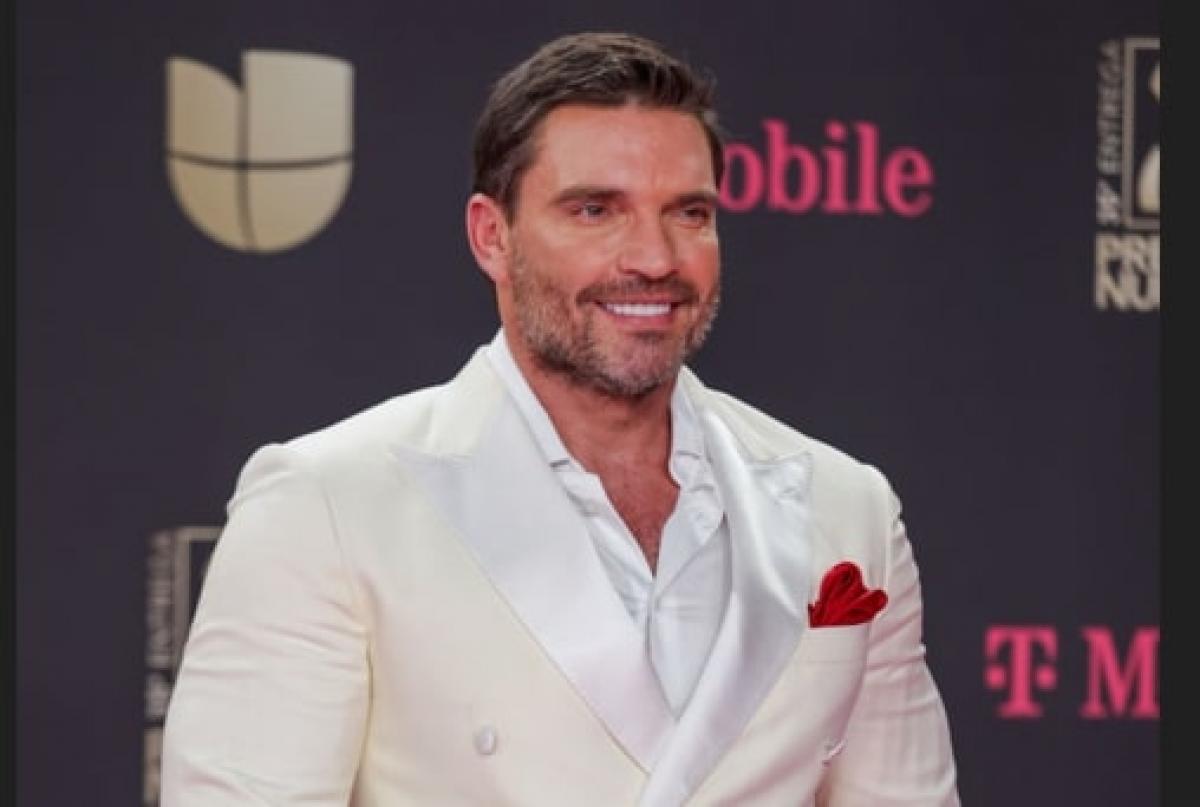 actor poartă un costum alb și zâmbește