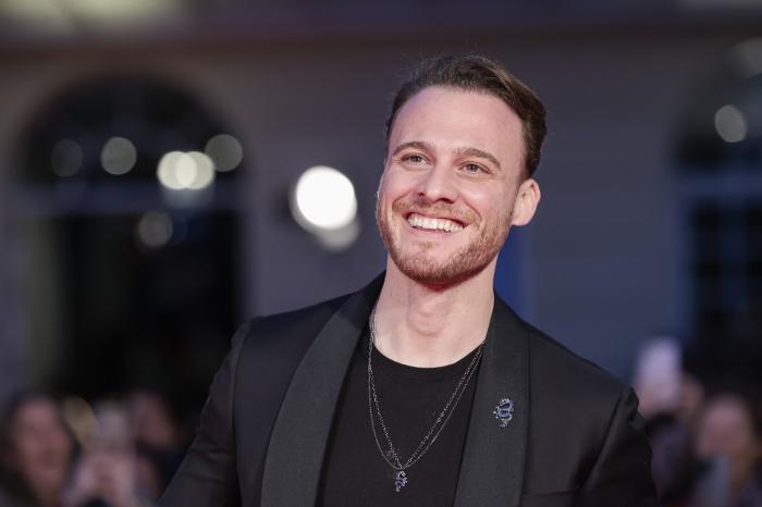 actor poartă o ținută all-black și zâmbește