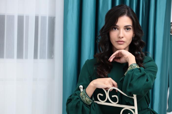 actriță poartă părul lung, desprins și rochie verde, stă pe scaun
