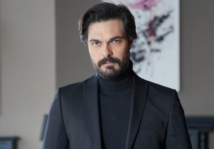 actor poartă o ținută all-black și zâmbește