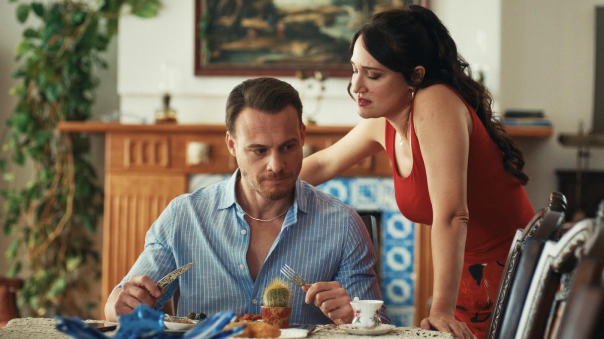 Kerem Bursin stă lângă o actriță pe platourile de filmare pe un fundal deschis la culoare