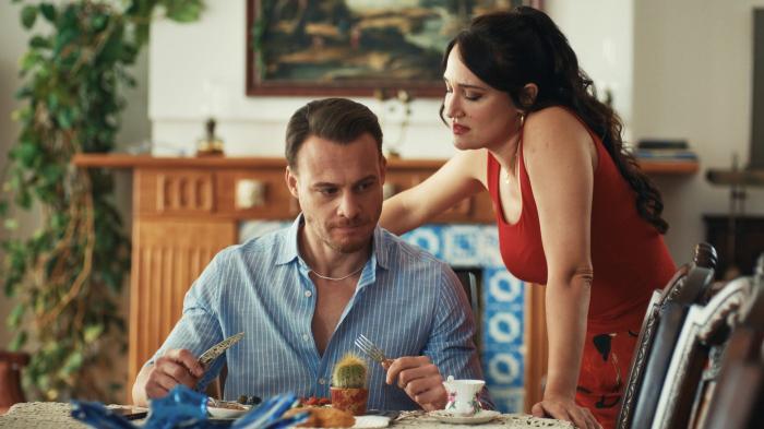 Kerem Bursin stă lângă o actriță pe platourile de filmare pe un fundal deschis la culoare