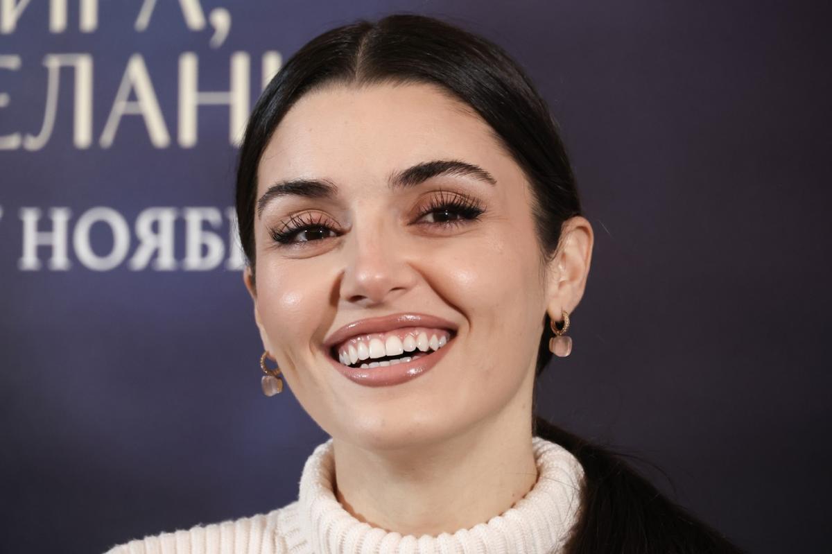 Hande Ercel zâmbește și poartă părul prins în coasă pe un fundal închis la culoare