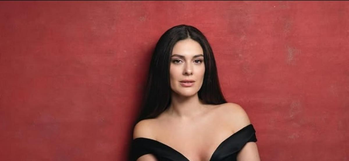 Berguzar Korel poartă o rochie neagră fără mâneci și părul lung desprins