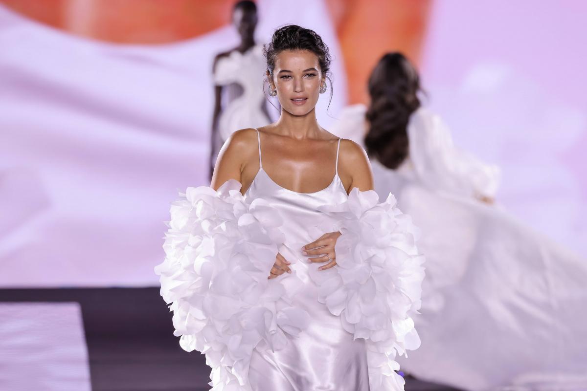 actriță îmbrăcată într-o rochie albă își ține mâinile pe burtica de gravidă