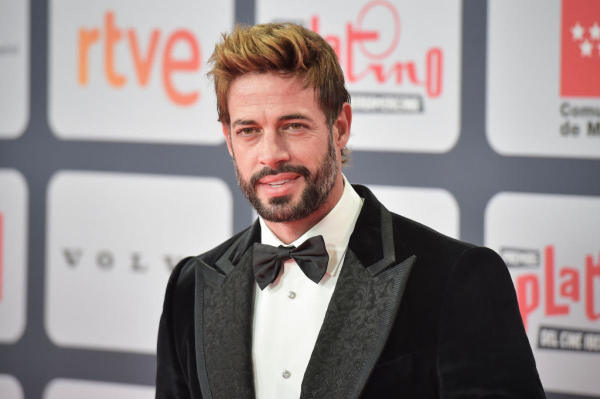 William Levy într-un costum negru zâmbește pe un fundal deschis la culoare