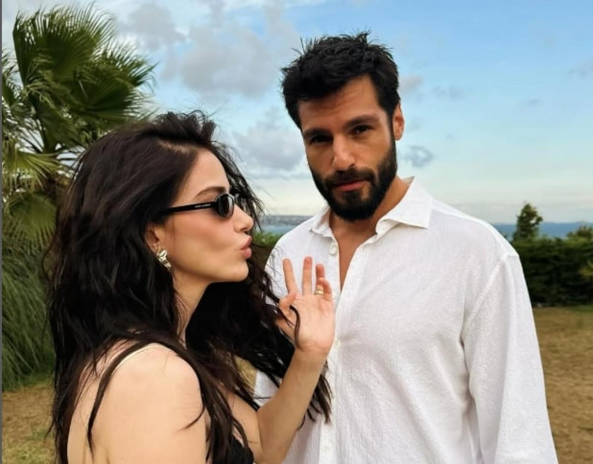 Serkan Cayoglu și Ozge Gurel stau unul lângă celălalt pe un fundal deschis la culoare