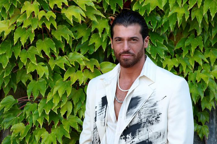 Can Yaman poartă un palton alb pe un fundal deschis la culoare