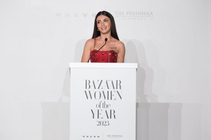 Ozge Yagiz poartă o rochie roșie fără mâneci și stă în fața unui microfon