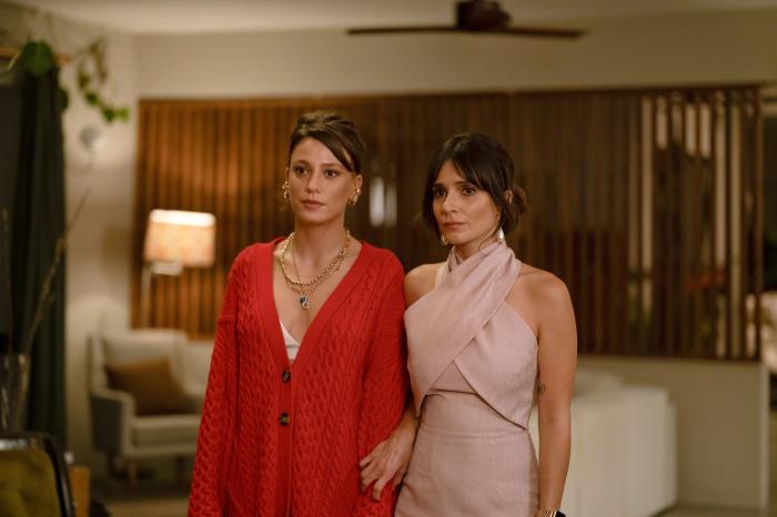 Serenay Sarikaya poartă o rochie roșie cu decolteu și stă lângă o colegă de platou pe un fundal deschis la culoare