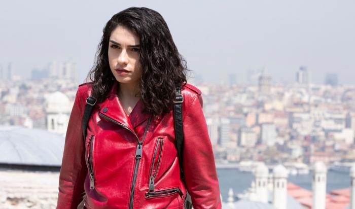 Hazar Erguclu poartă o geacă de blugi roșie și are părul brunet desprins