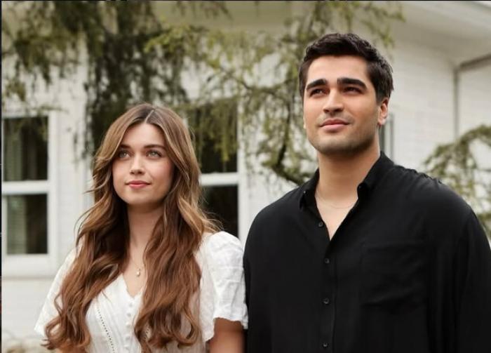 Afra Saracoglu poartă părul lung desprins și Mert Ramazan Demir poartă o bluză neagră pe un fundal deschis la culoare