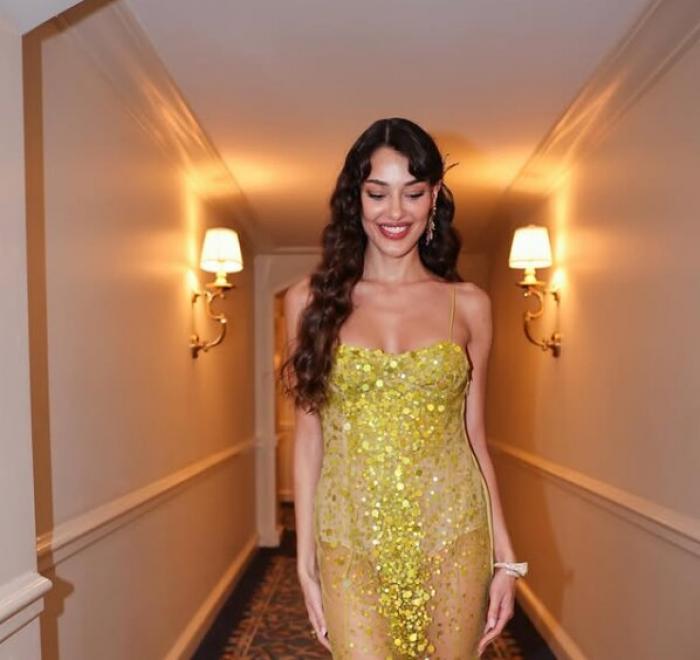 Dilan Cicek Deniz poartă o rochie galbenă fără mâneci și părul lung și zâmbește