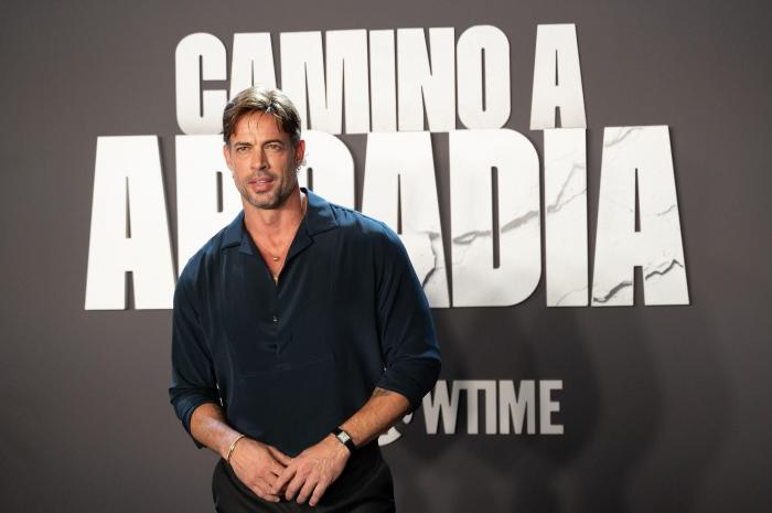 william Levy poartă o cămașă închisă la culoare pe un fundal deschis