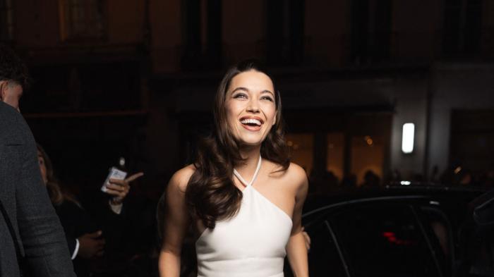 Afra Saracoglu poartă o rochie albă fără mâneci și zâmbește